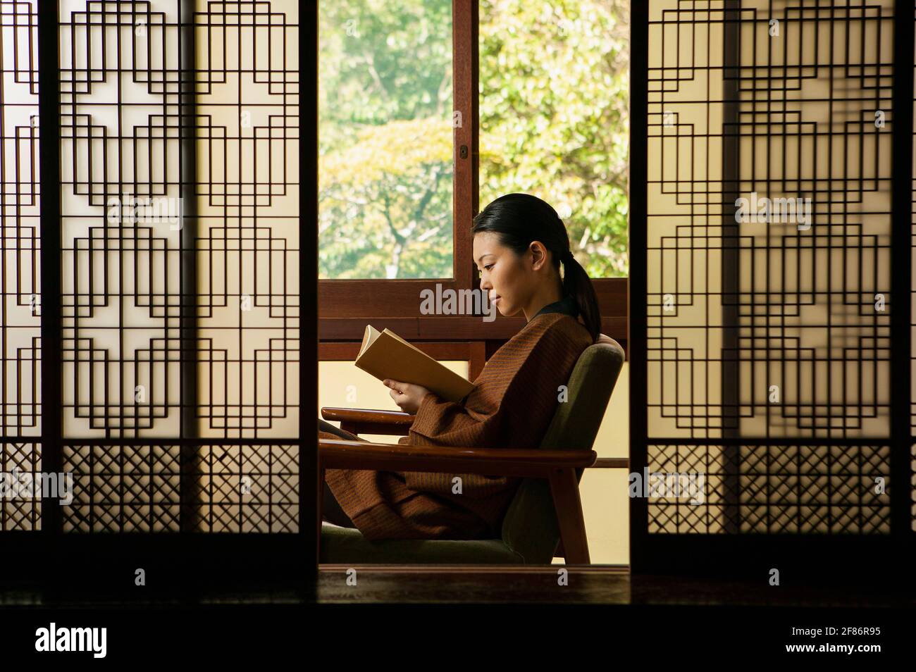 Ruhige junge Frau, die hinter gemusterten Shoji-Türen ein Buch liest Stockfoto