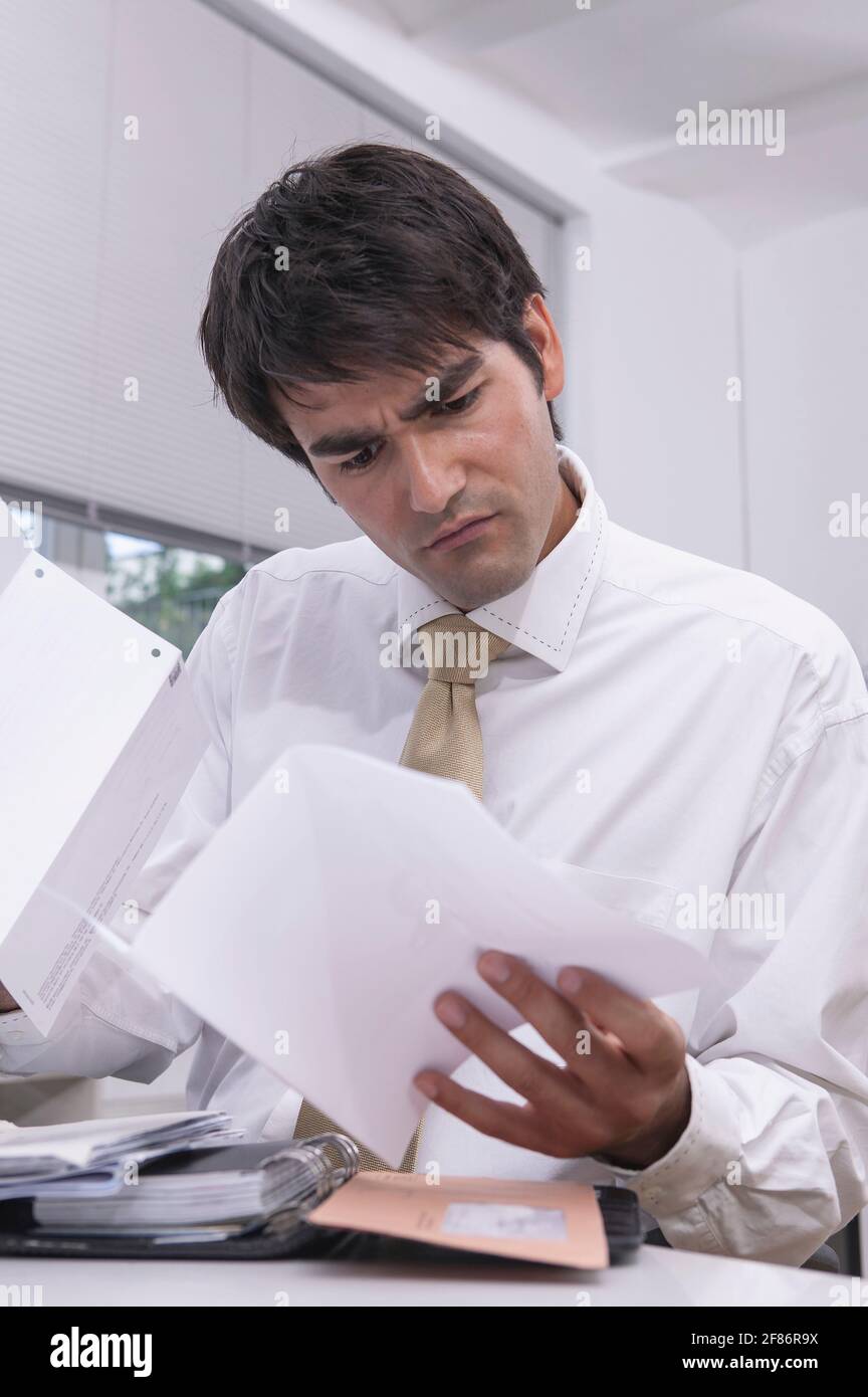 Verwirrt Geschäftsmann Überprüfung Papiere im Büro Stockfoto