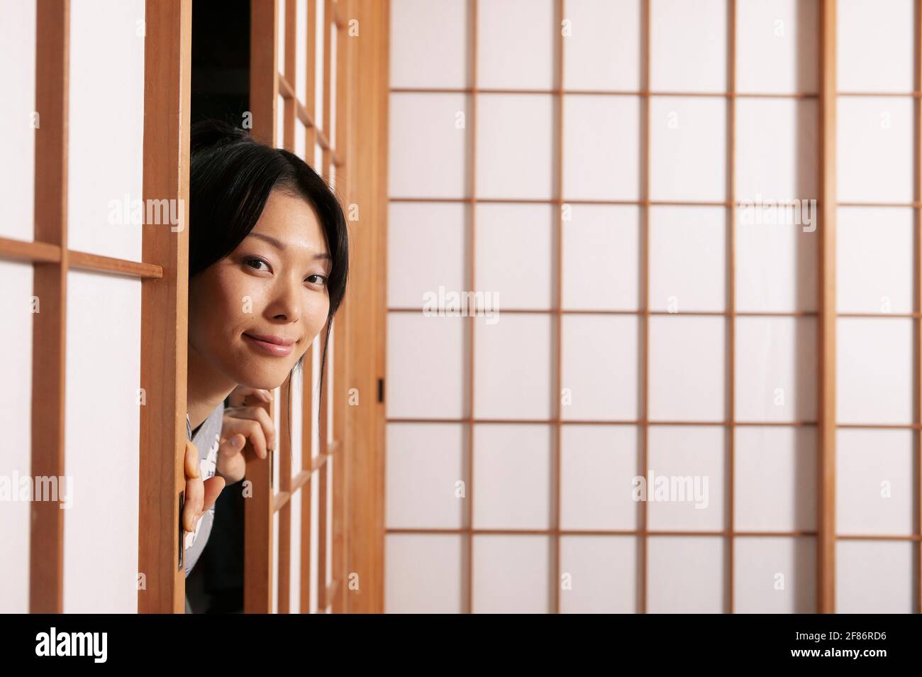 Portrait schöne junge Frau, die hinter Shoji-Türen gucken Stockfoto