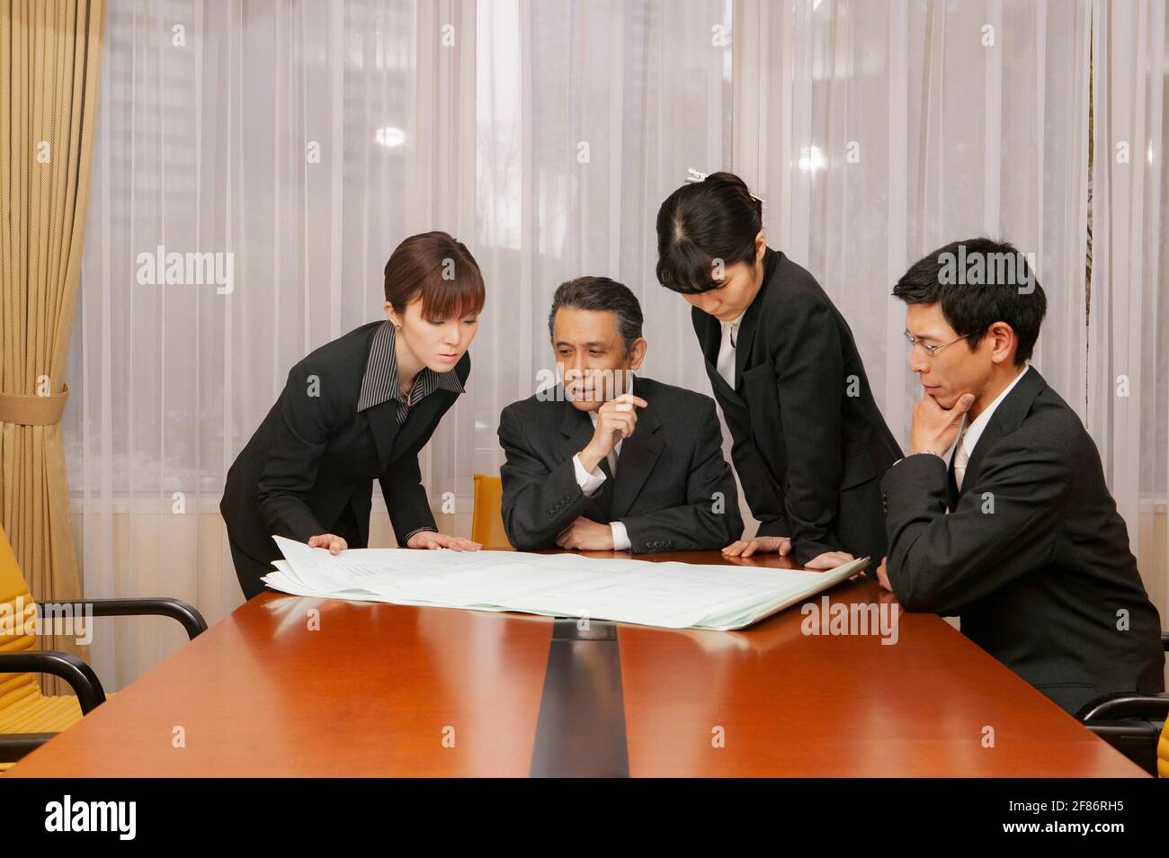 Geschäftsleute, die sich im Konferenzraum des Büros die Blaupausen durcharbeiten Stockfoto