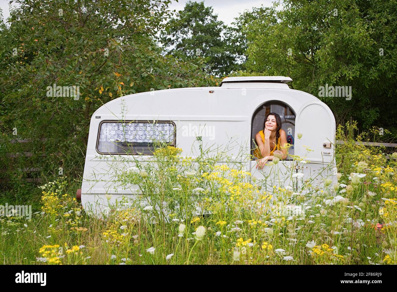 Junge Frau, die sich im Wohnwagen auf einer idyllischen Wiese entspannt Stockfoto