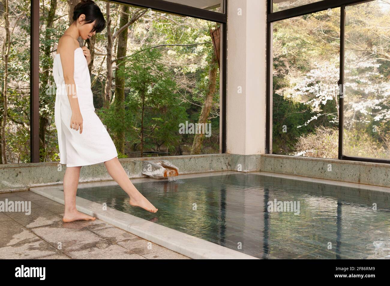 Junge Frau in einem Handtuch, die bei Onsen den Zeh in Wasser taucht Stockfoto