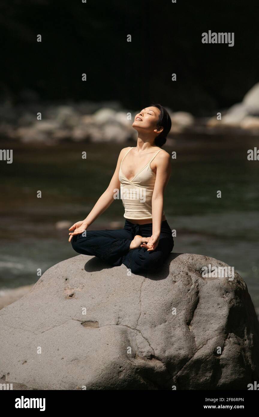 Ruhige, schöne junge Frau, die in Lotushaltung bei Sonnenschein meditiert Rock Stockfoto
