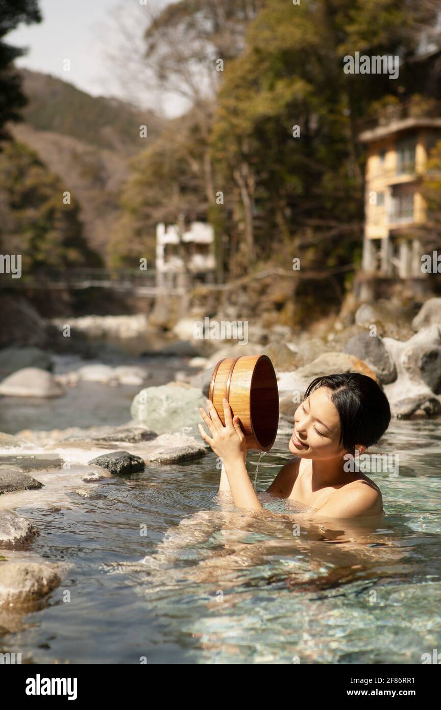 Glückliche junge Frau mit Eimer im sonnigen Pool in Onsen, Izu, Japan Stockfoto