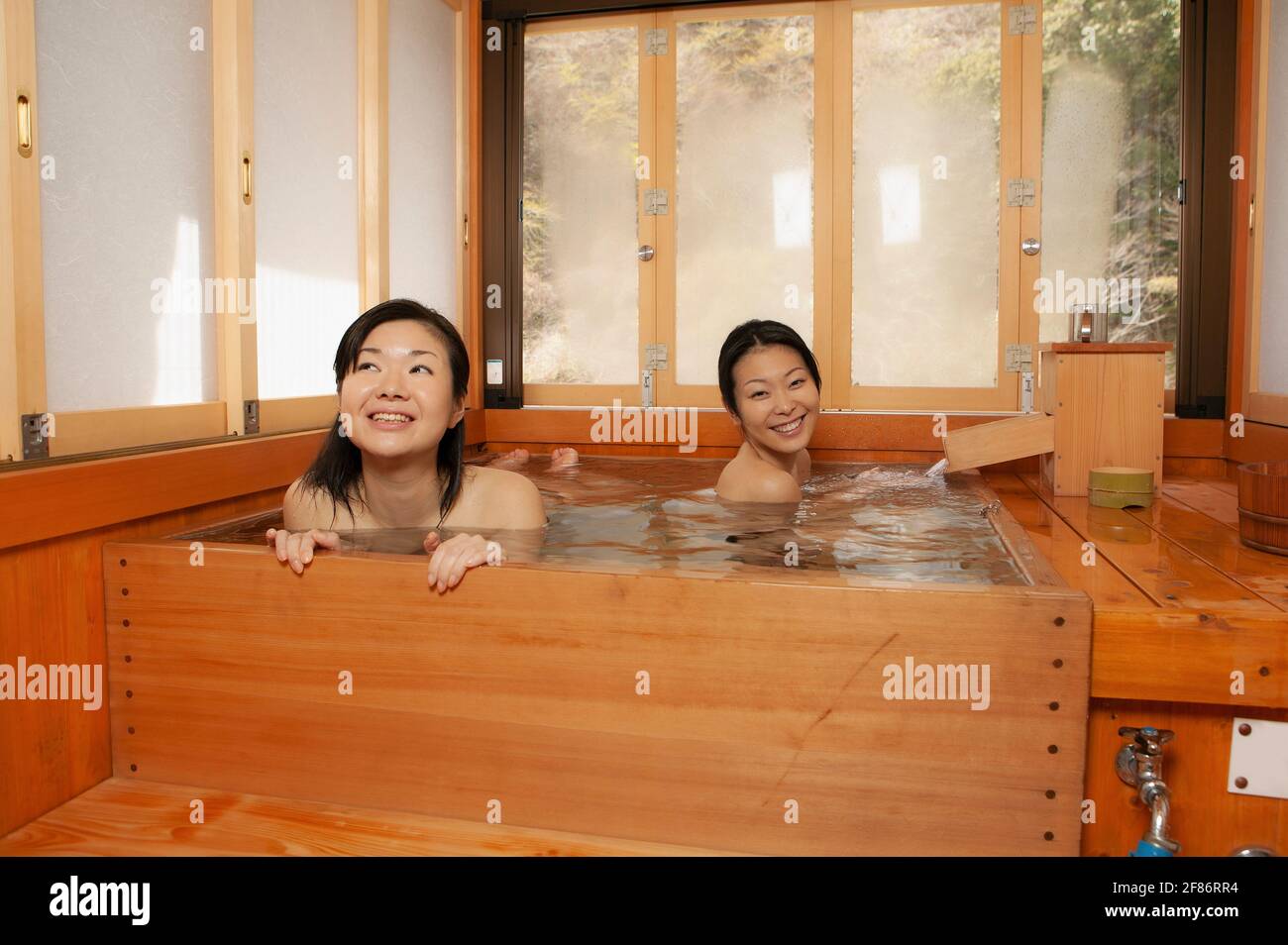 Fröhliche junge Freundinnen, die in einem Holzpool in Onsen baden Stockfoto