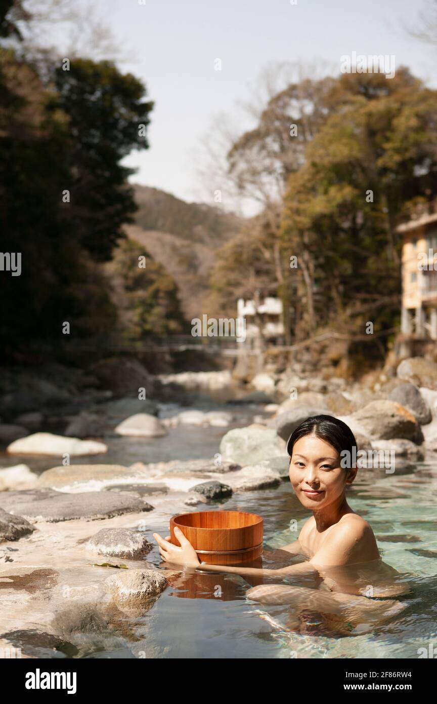 Portrait schöne junge Frau mit Eimer in sonnigen Pool an Onsen Stockfoto