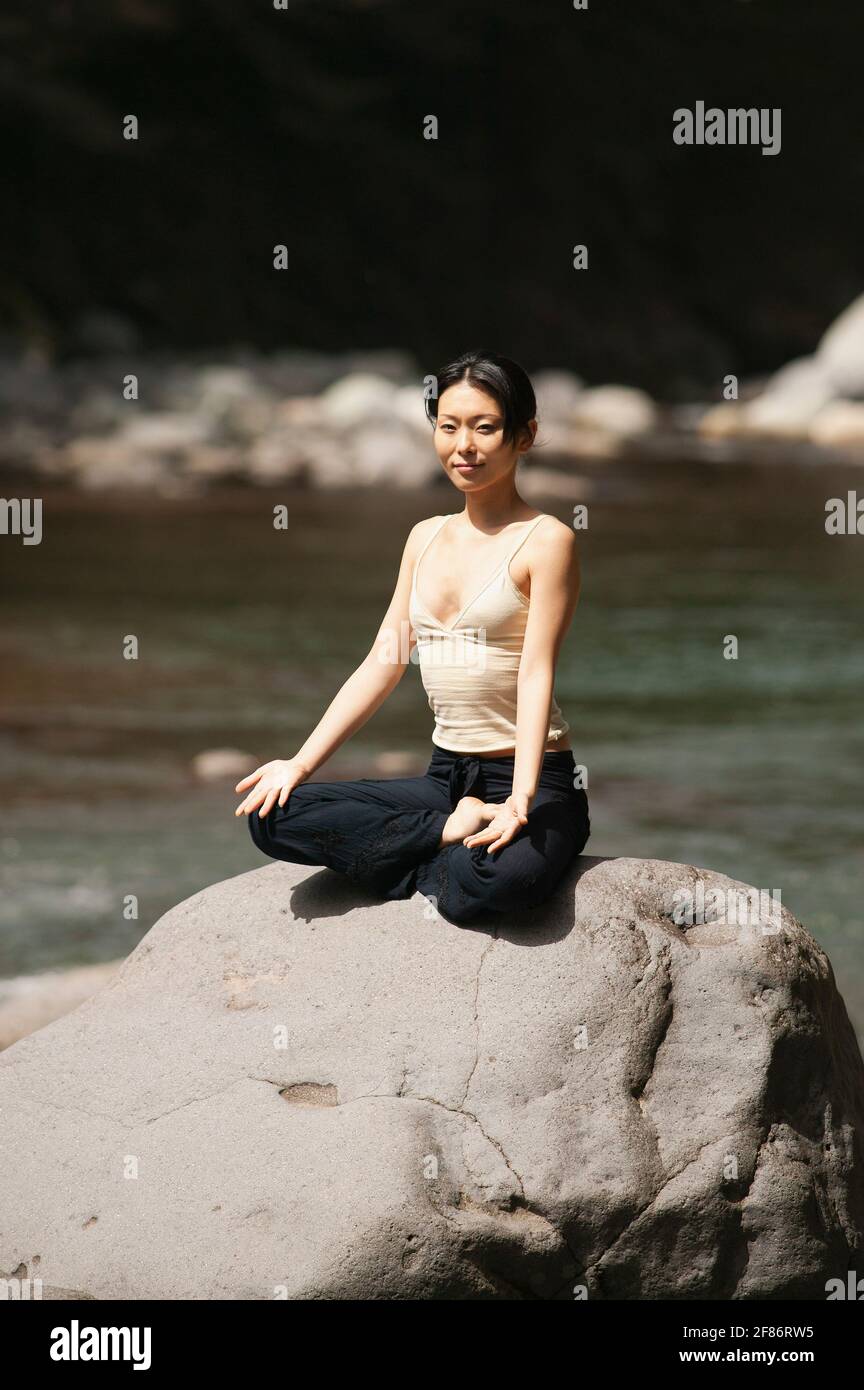 Portrait schöne junge Frau, die in Lotushaltung bei Sonnenschein meditiert Rock Stockfoto