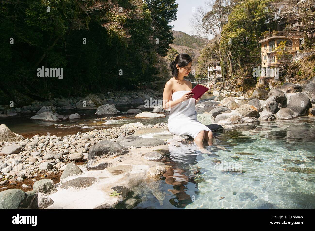 Junge Frau im Buch mit Handtüchern am sonnigen Pool in Onsen, Izu, Japan Stockfoto
