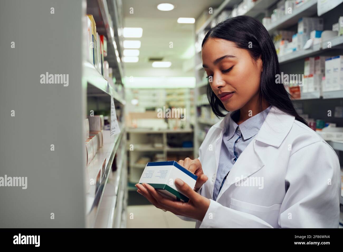 Junge Apothekerin liest Anweisungen auf der Arzneischachtel, die darin steht Gang der Apotheke Stockfoto