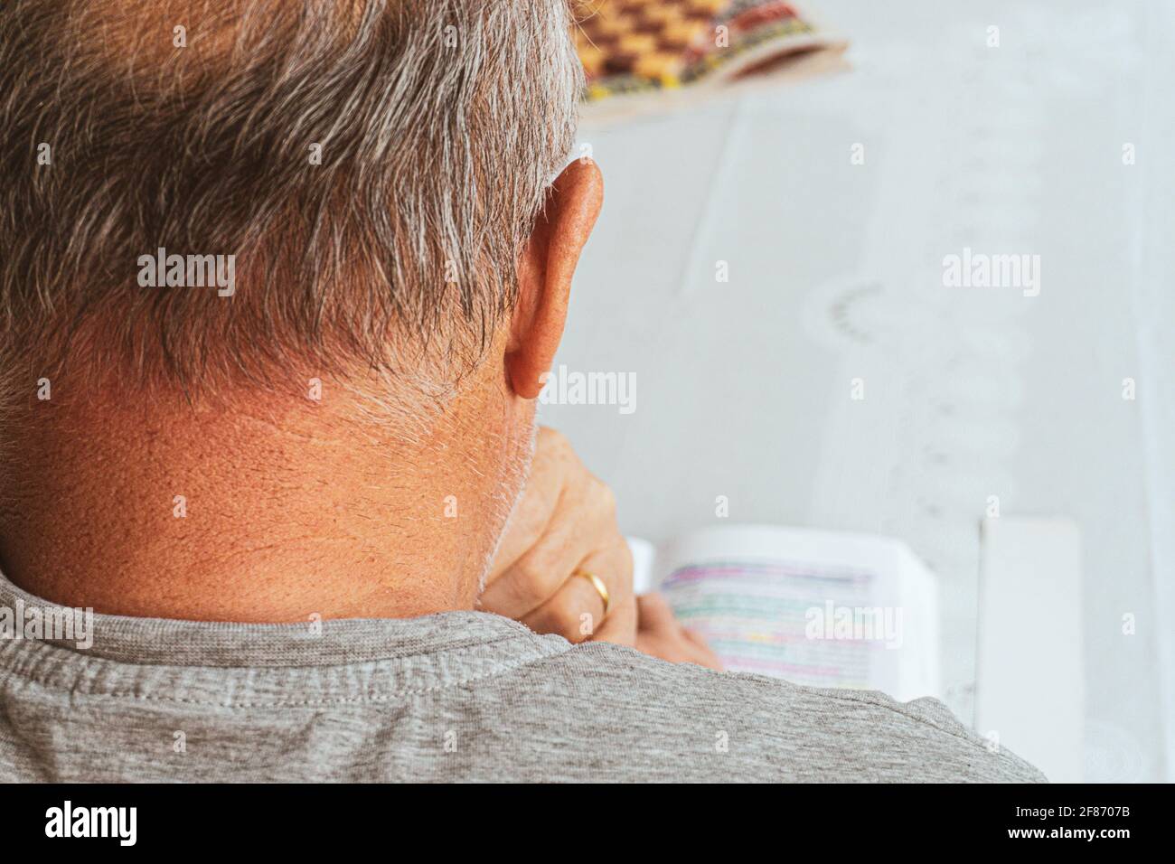 Der alte Mann liest Buch auf dem Tisch. Kulturelles Aktivitätskonzept mit einer Person. Stockfoto