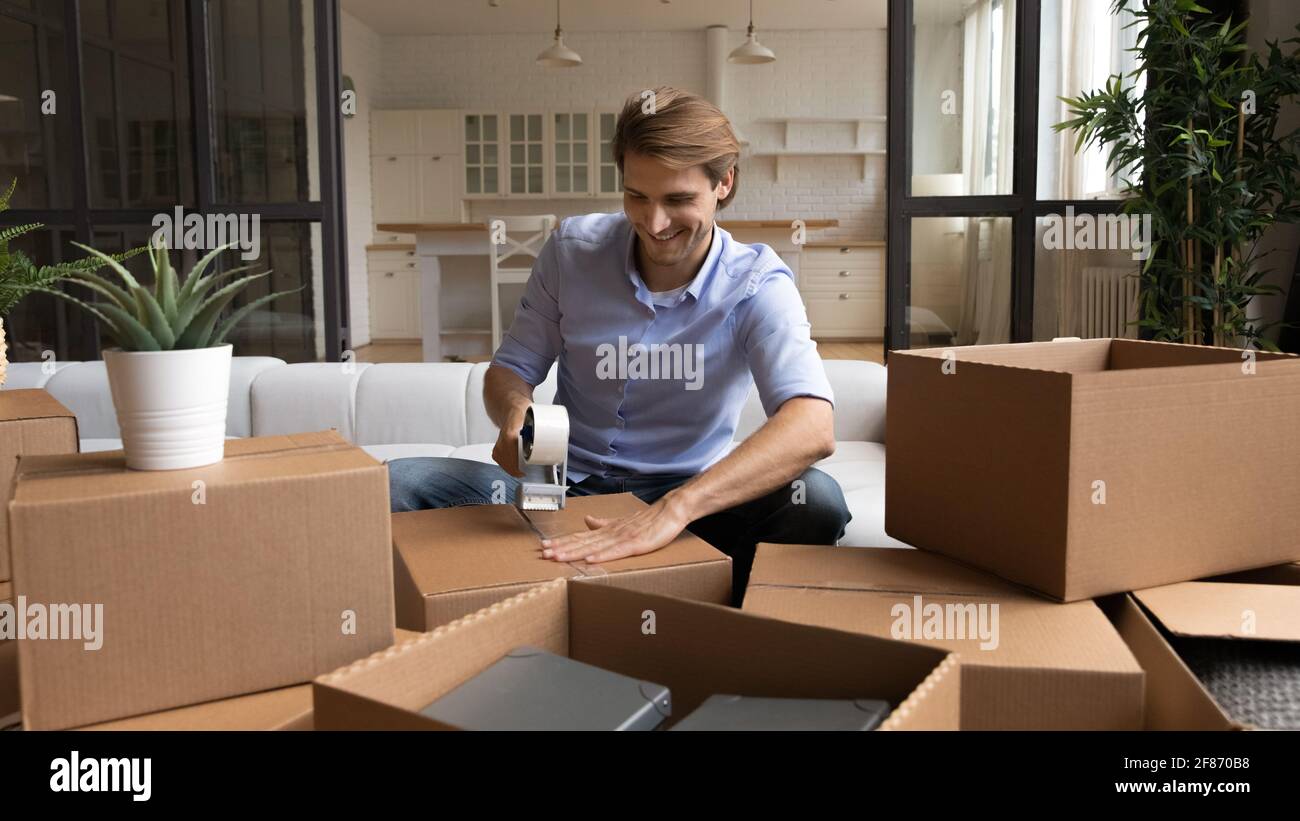 Lächelnder Mann, der Pappkartons zu Hause mit Klebeband verpackt Stockfoto