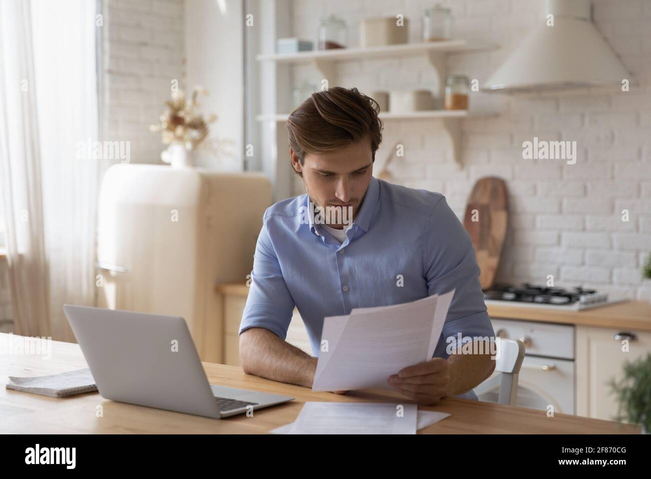 Fokussierter Mann, der mit Dokumenten arbeitet und mit einem Laptop am Tisch sitzt Stockfoto