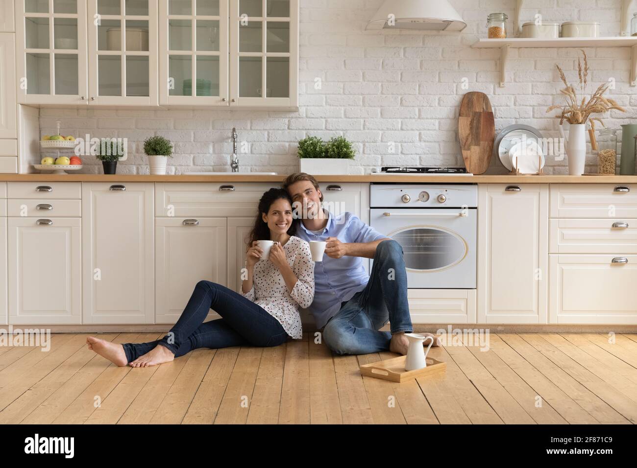 Portrait glückliche Familie, die Tee trinkt, auf warmem Küchenboden sitzt Stockfoto