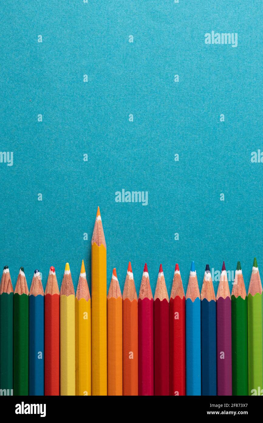 Draufsicht. Farbige Bleistifte nebeneinander auf blauem Hintergrund mit einer Textur, die den gelben Bleistift hervorhebt. Stockfoto
