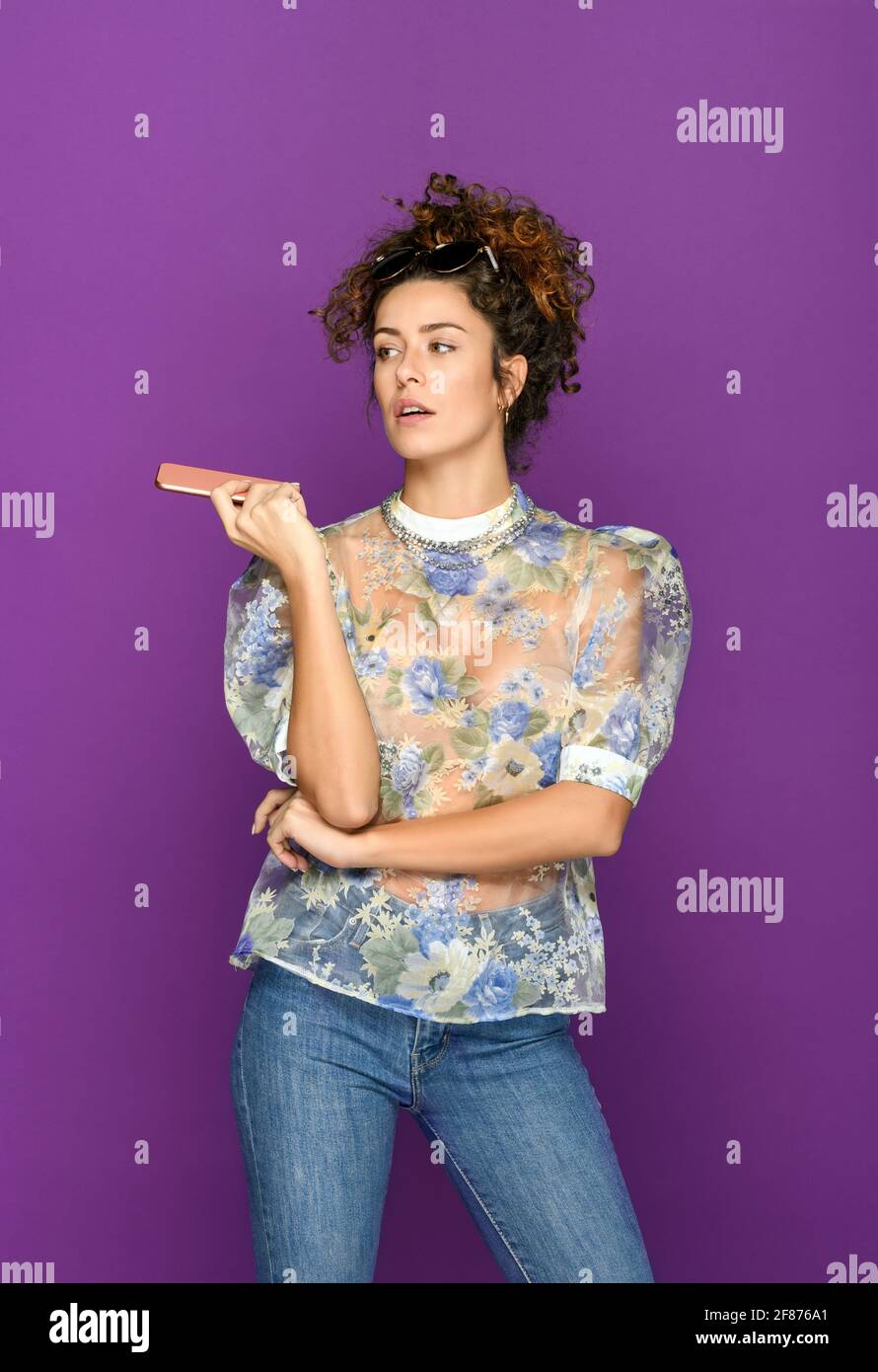 Trendige selbstbewusste Frau mit Mobiltelefon, das sich absieht Heller violetter Hintergrund Stockfoto