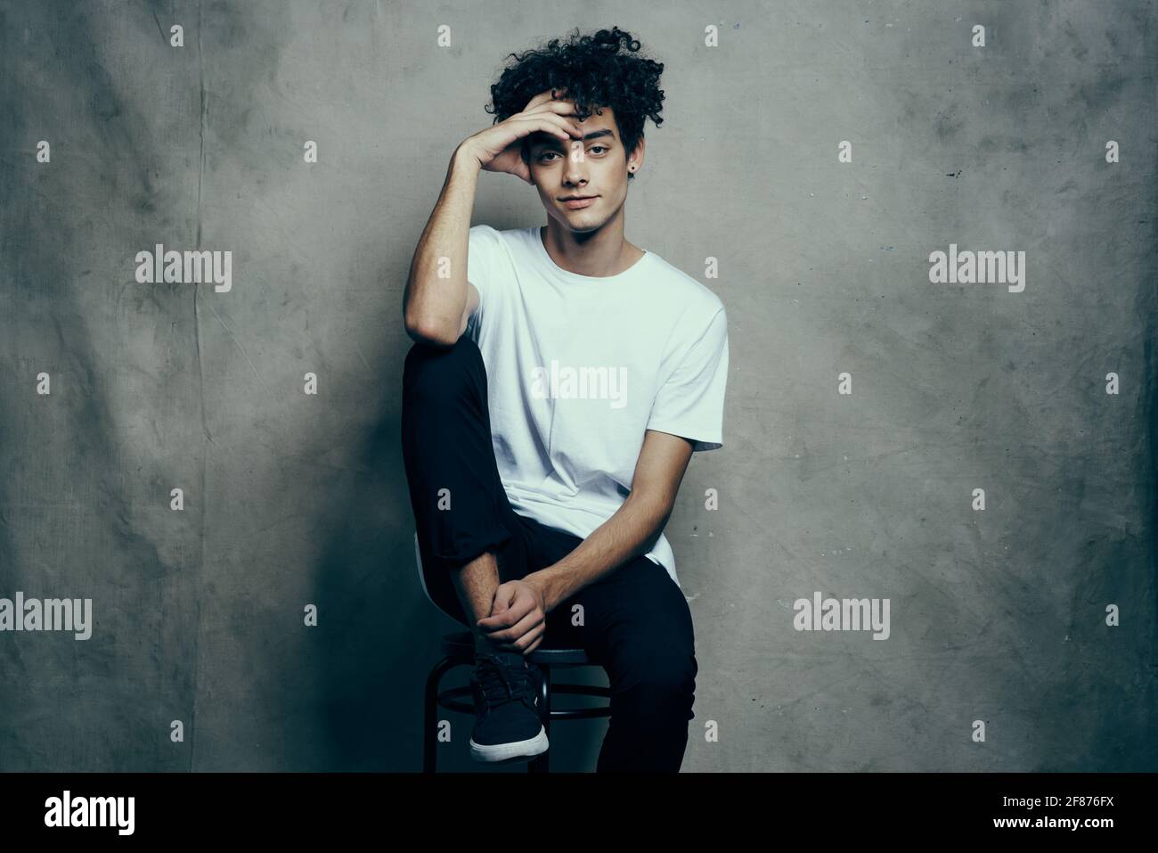 Mann in weißem T-Shirt sitzt auf Stühlen Mode lockiges Haar Lifestyle Stockfoto