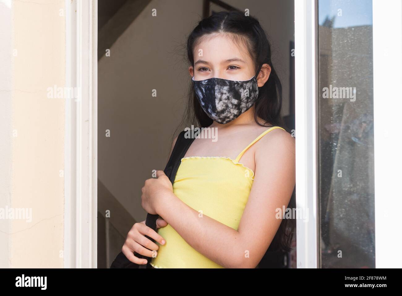 Nahaufnahme eines kleinen hispanischen Mädchens mit Maske Lehnt sich an die Tür Stockfoto