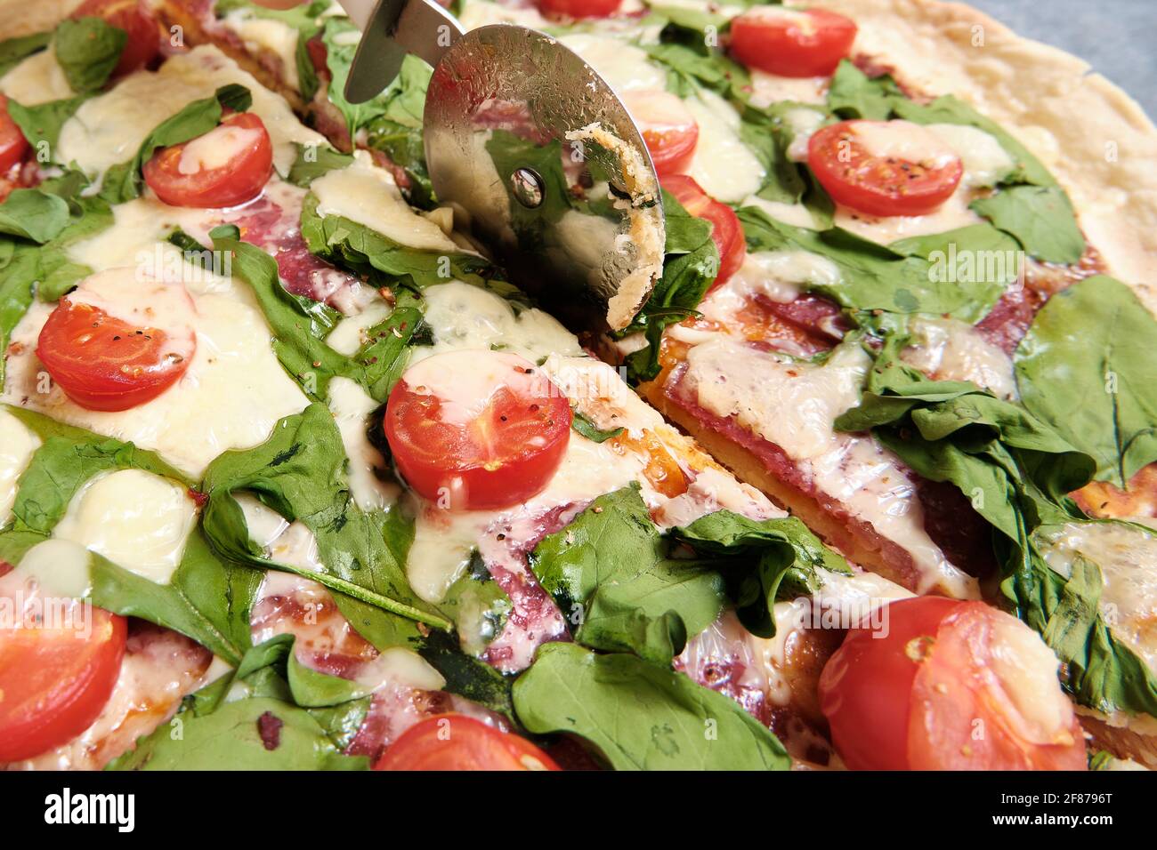 Pizza mit Käse, Tomaten, Spinat und Räucherwurst Stockfoto