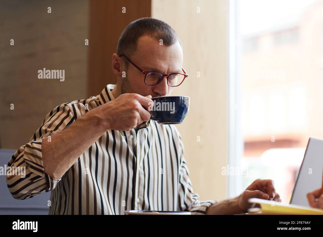 Minimalporträt eines jungen Geschäftsmannes, der Kaffee trinkt, während er mit einem Laptop am Tisch im Café arbeitet, Kopierraum Stockfoto