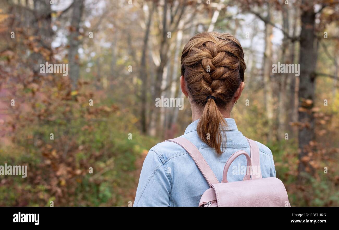 Mädchen in einem Jeanshemd mit Rucksack auf dem Hintergrund des Herbstwaldes. Nahaufnahme. Rückansicht einer jungen Frau mit Sense. Speicherplatz kopieren. Stockfoto