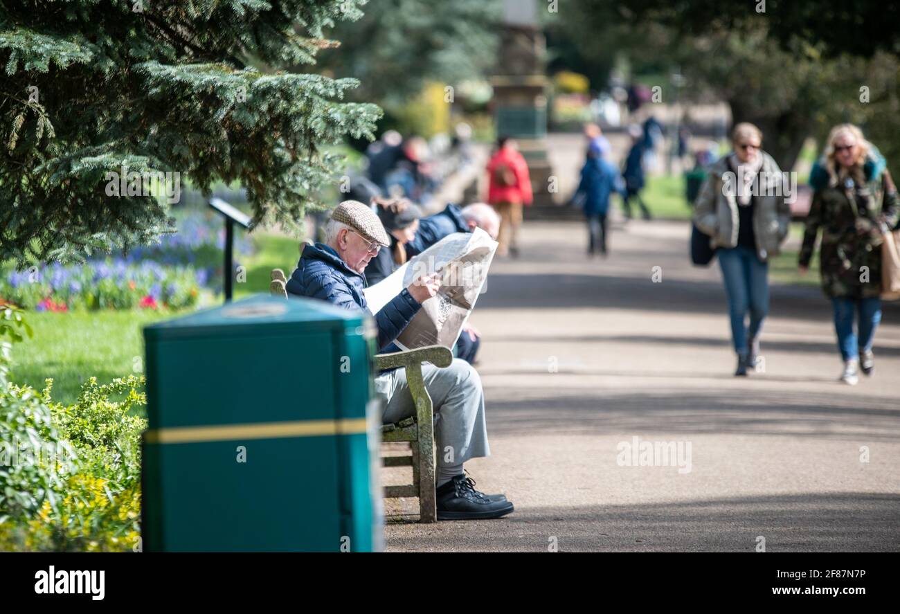 Leamington Spa, 12. April 2021: Ein älterer Herr nutzt den Sonneneinbruch heute Morgen, um seine Zeitung im Jephson Gardens Park zu lesen. Kredit: Ryan Underwood / Alamy Live Nachrichten Stockfoto