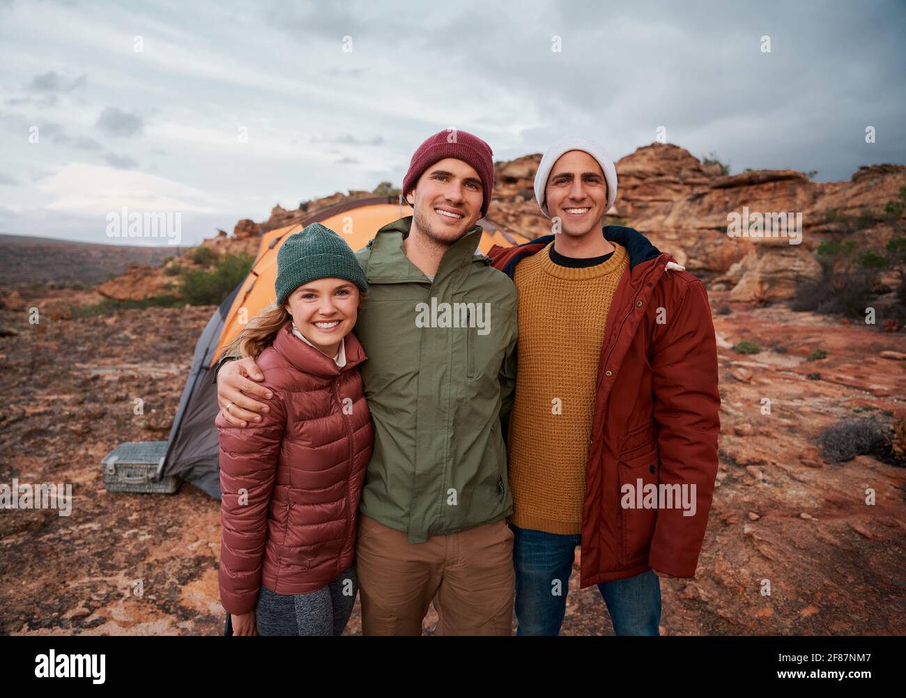 Eine Gruppe junger, glücklicher Freunde, die während des Aufstellens vor dem Zelt stehen Camping in Winterkleidung Stockfoto