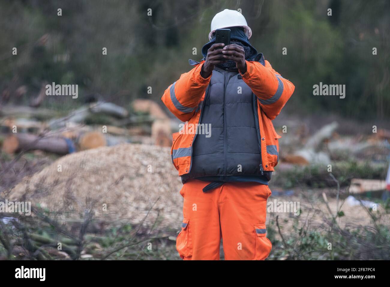 Wendover, Großbritannien. 9.. April 2021. Ein HS2-Mitarbeiter verwendet ein Mobiltelefon, um einen Pressefotografen auf dem Gelände der ehemaligen Road Barn Farm neben der A413 zu Filmen, auf der kürzlich Bäume für die Hochgeschwindigkeitsstrecke von HS2 gefällt wurden. Die Arbeit am Holzfäller für das Projekt findet nun an mehreren Standorten zwischen Great Missenden und Wendover im Chilterns AONB statt, unter anderem in Jones Hill Wood. Kredit: Mark Kerrison/Alamy Live Nachrichten Stockfoto