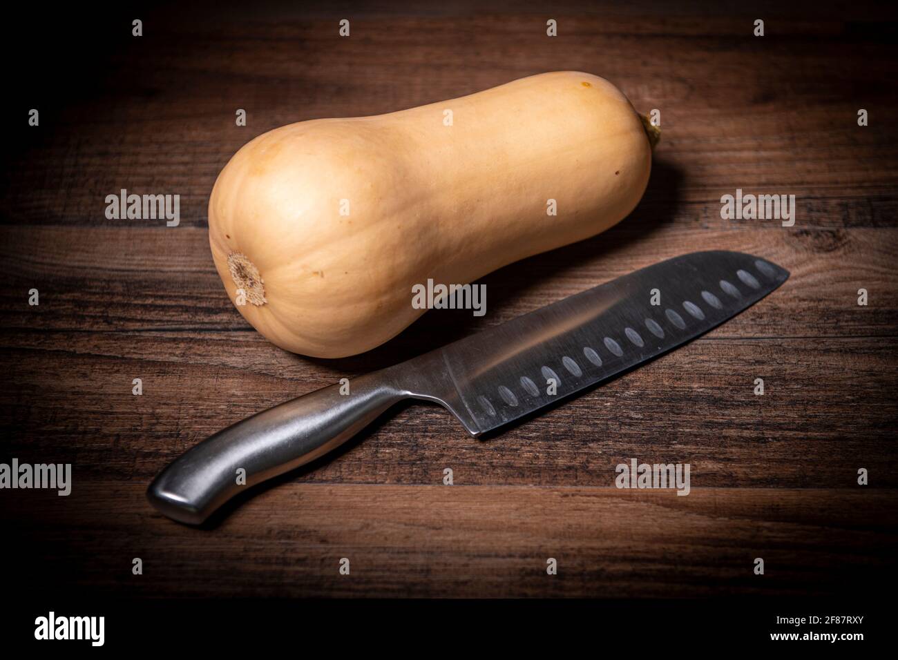 Ganze Butternut mit einem Messer auf einer Holzplatte zusammendrücken. Stockfoto
