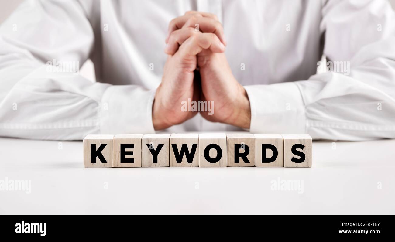 Das Wort Schlüsselwörter auf Holzwürfel mit einem Geschäftsmann mit Spange Hände Hintergrund geschrieben. Suchmaschinenoptimierung und Online-Marketing-Konzept. Stockfoto