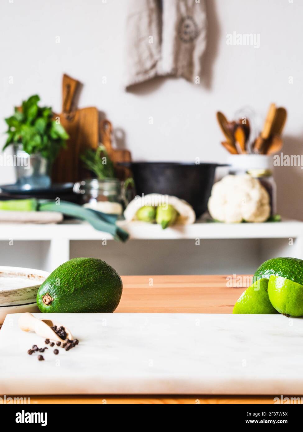 Holztisch mit grünem Obst und Marmorplatte und verschwommenem Küchenhintergrund. Copyspace. Konzept der Lebensmittelzubereitung, Küche im Hintergrund. Stockfoto