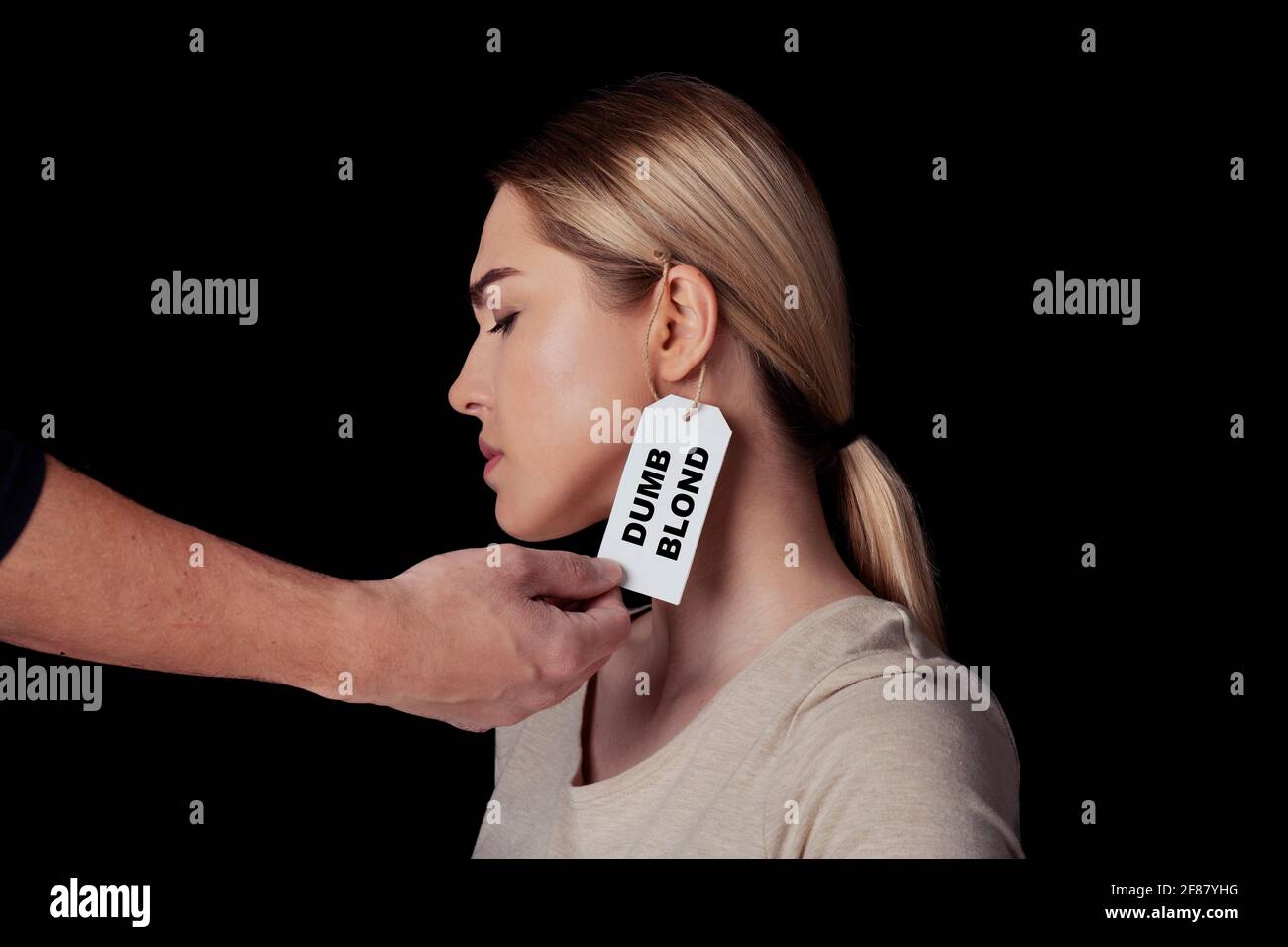 Hand des Mannes berühren Gesicht der verärgerten jungen Frau mit Label auf dem Ohr ist stumm blond Stockfoto