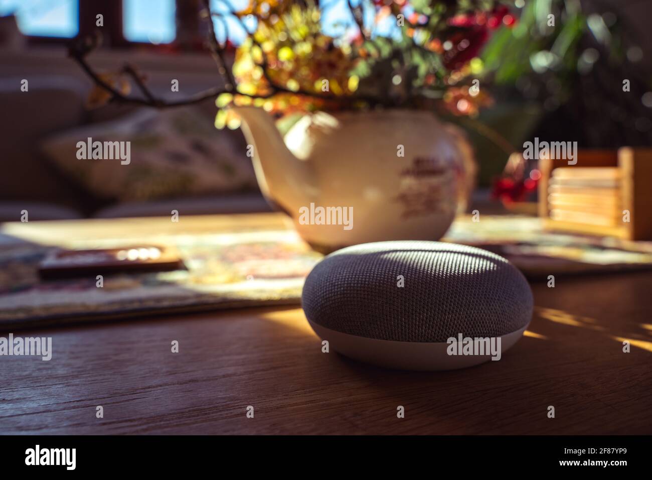 Sprachgesteuerter intelligenter Lautsprecher mit einer Frau im Hintergrund in einer Innenraumumgebung. Intelligentes AI-Lautsprecherkonzept Stockfoto