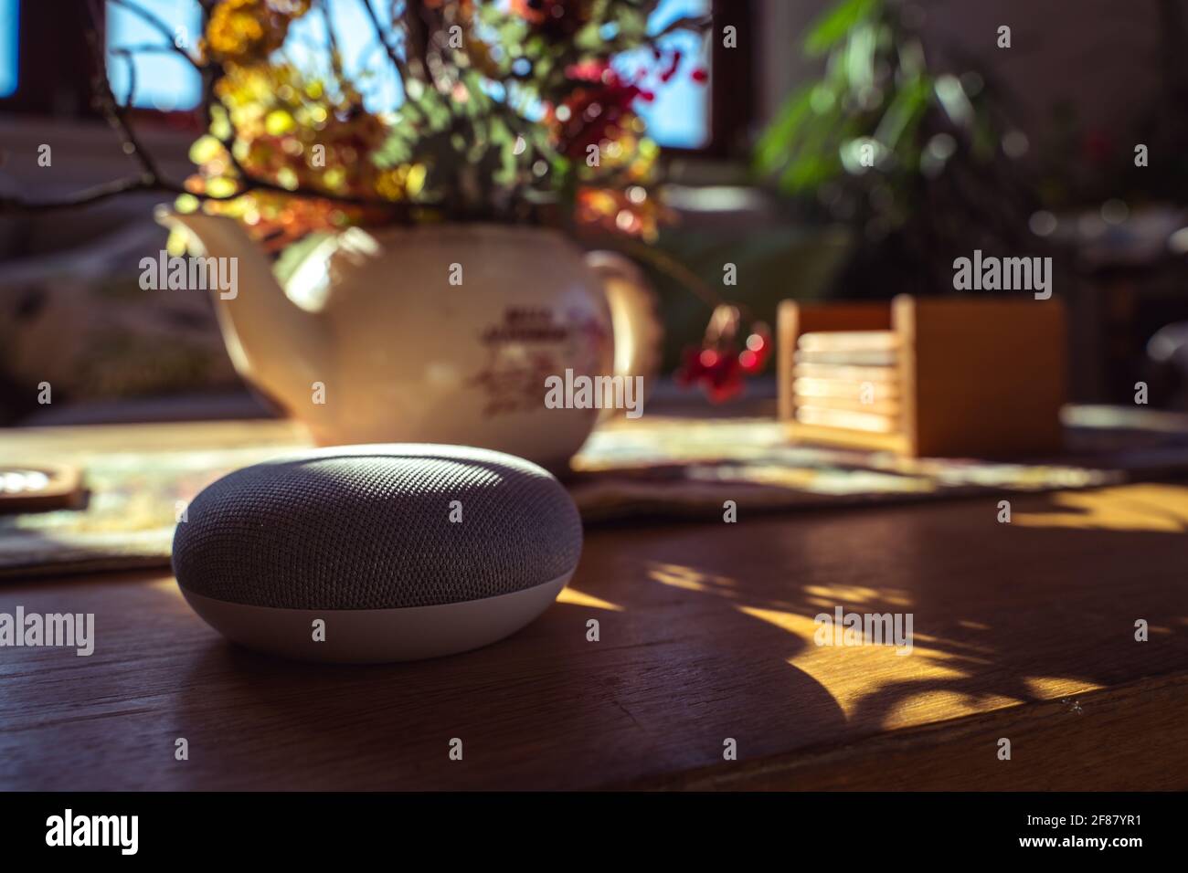 Sprachgesteuerter intelligenter Lautsprecher mit einer Frau im Hintergrund in einer Innenraumumgebung. Intelligentes AI-Lautsprecherkonzept Stockfoto