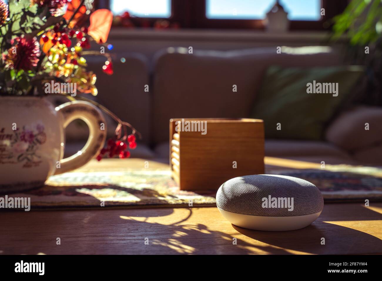 Sprachgesteuerter intelligenter Lautsprecher mit einer Frau im Hintergrund in einer Innenraumumgebung. Intelligentes AI-Lautsprecherkonzept Stockfoto