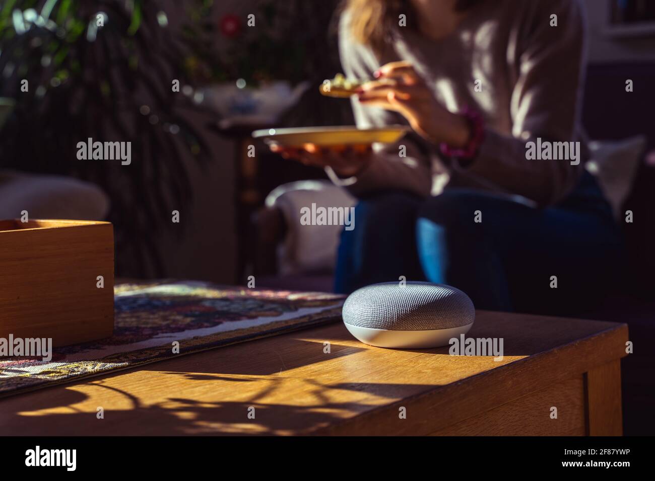 Sprachgesteuerter intelligenter Lautsprecher mit einer Frau im Hintergrund in einer Innenraumumgebung. Intelligentes AI-Lautsprecherkonzept Stockfoto