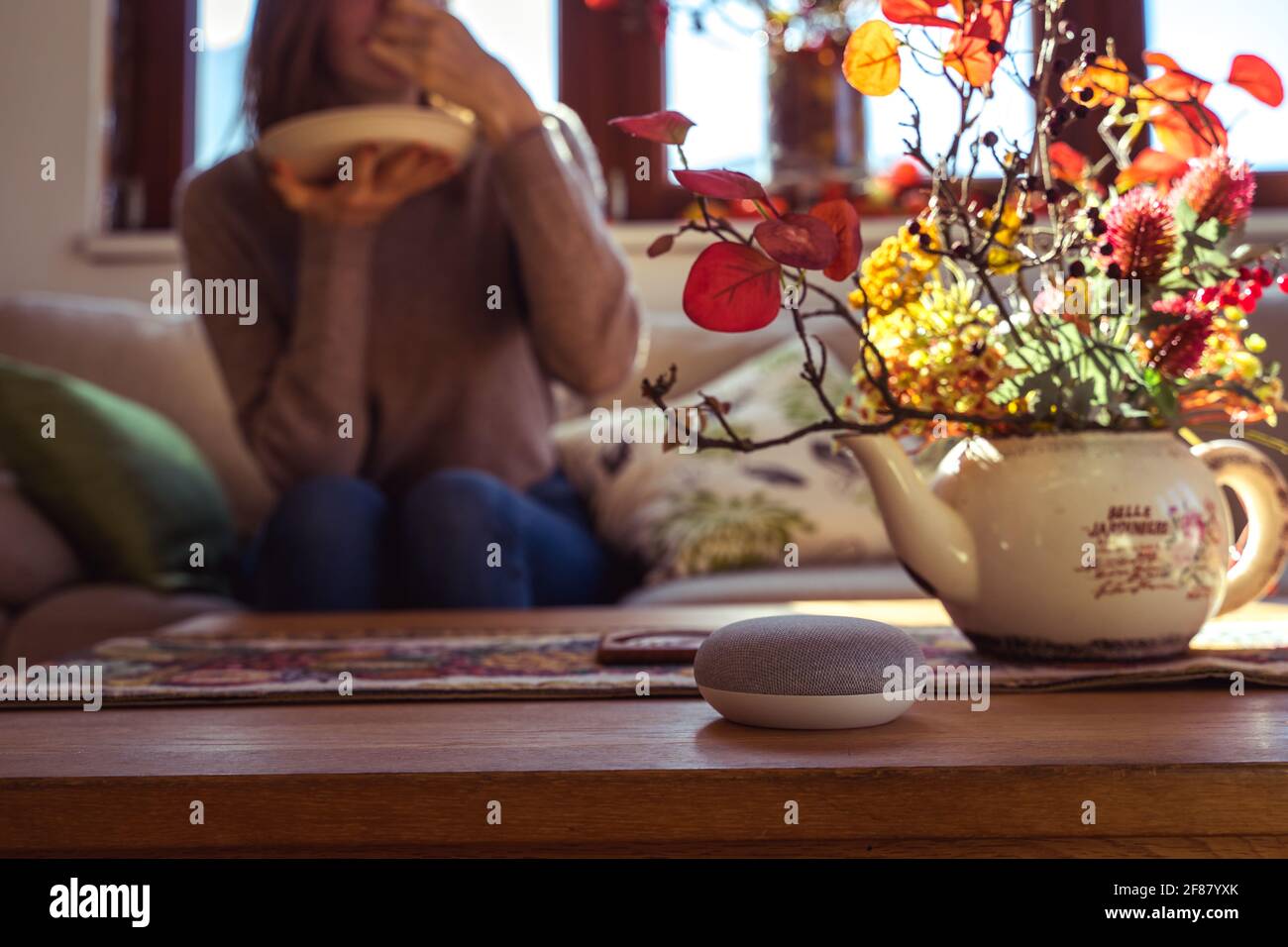 Sprachgesteuerter intelligenter Lautsprecher mit einer Frau im Hintergrund in einer Innenraumumgebung. Intelligentes AI-Lautsprecherkonzept Stockfoto
