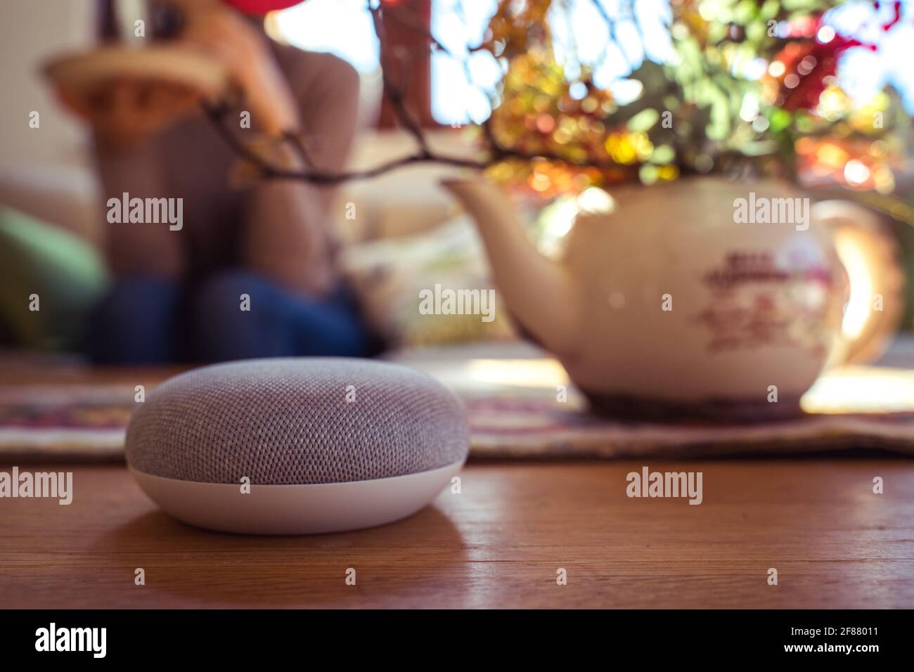 Sprachgesteuerter intelligenter Lautsprecher mit einer Frau im Hintergrund in einer Innenraumumgebung. Intelligentes AI-Lautsprecherkonzept Stockfoto