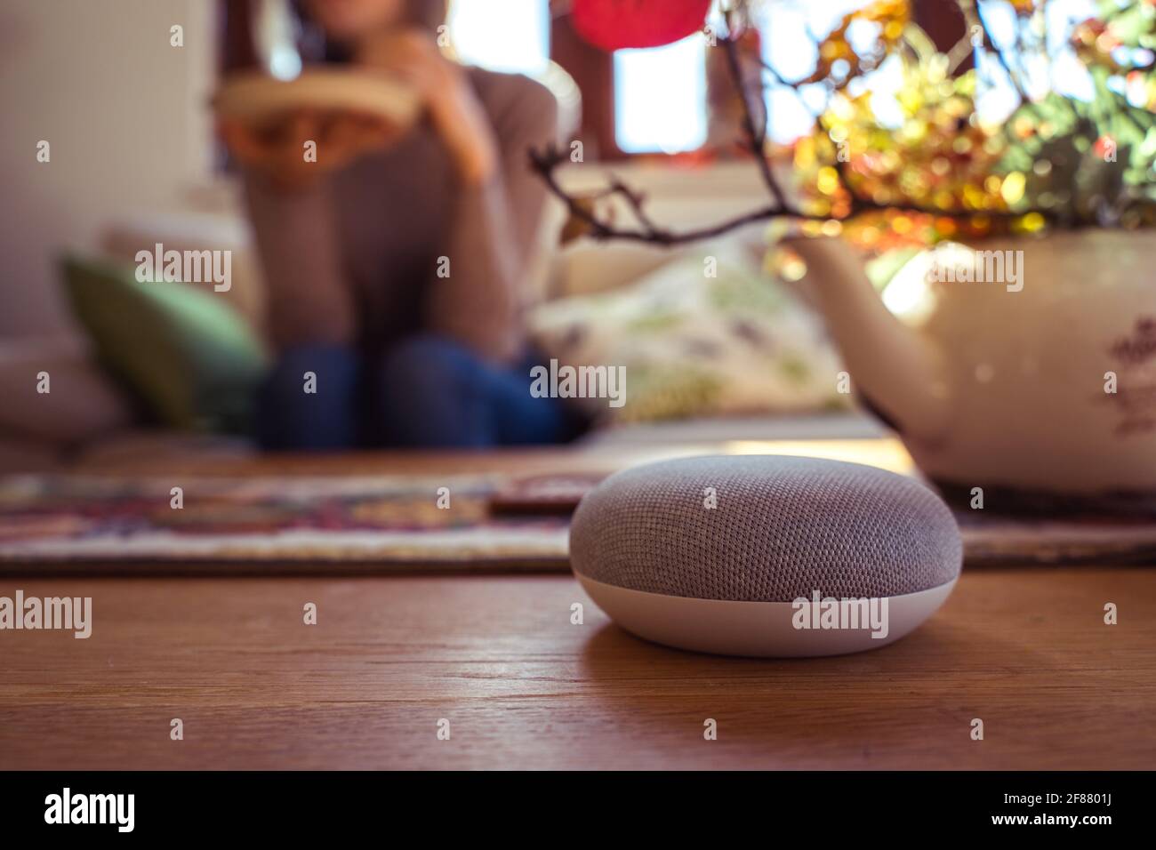 Sprachgesteuerter intelligenter Lautsprecher mit einer Frau im Hintergrund in einer Innenraumumgebung. Intelligentes AI-Lautsprecherkonzept Stockfoto