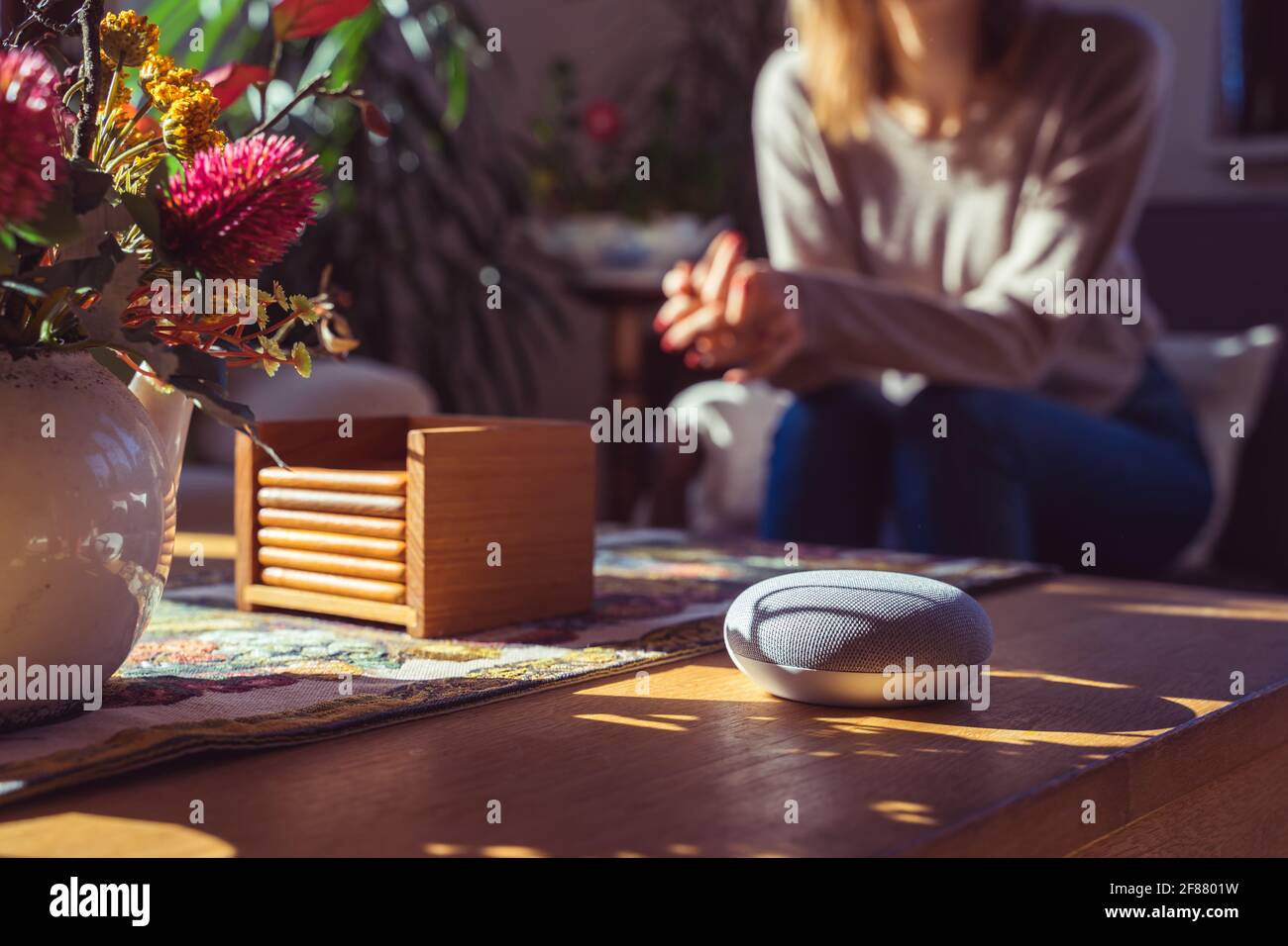 Sprachgesteuerter intelligenter Lautsprecher mit einer Frau im Hintergrund in einer Innenraumumgebung. Intelligentes AI-Lautsprecherkonzept Stockfoto