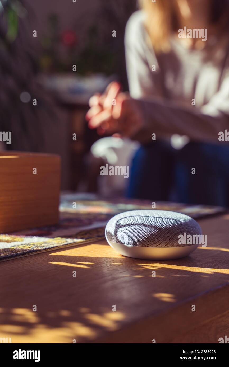Sprachgesteuerter intelligenter Lautsprecher mit einer Frau im Hintergrund in einer Innenraumumgebung. Intelligentes AI-Lautsprecherkonzept Stockfoto