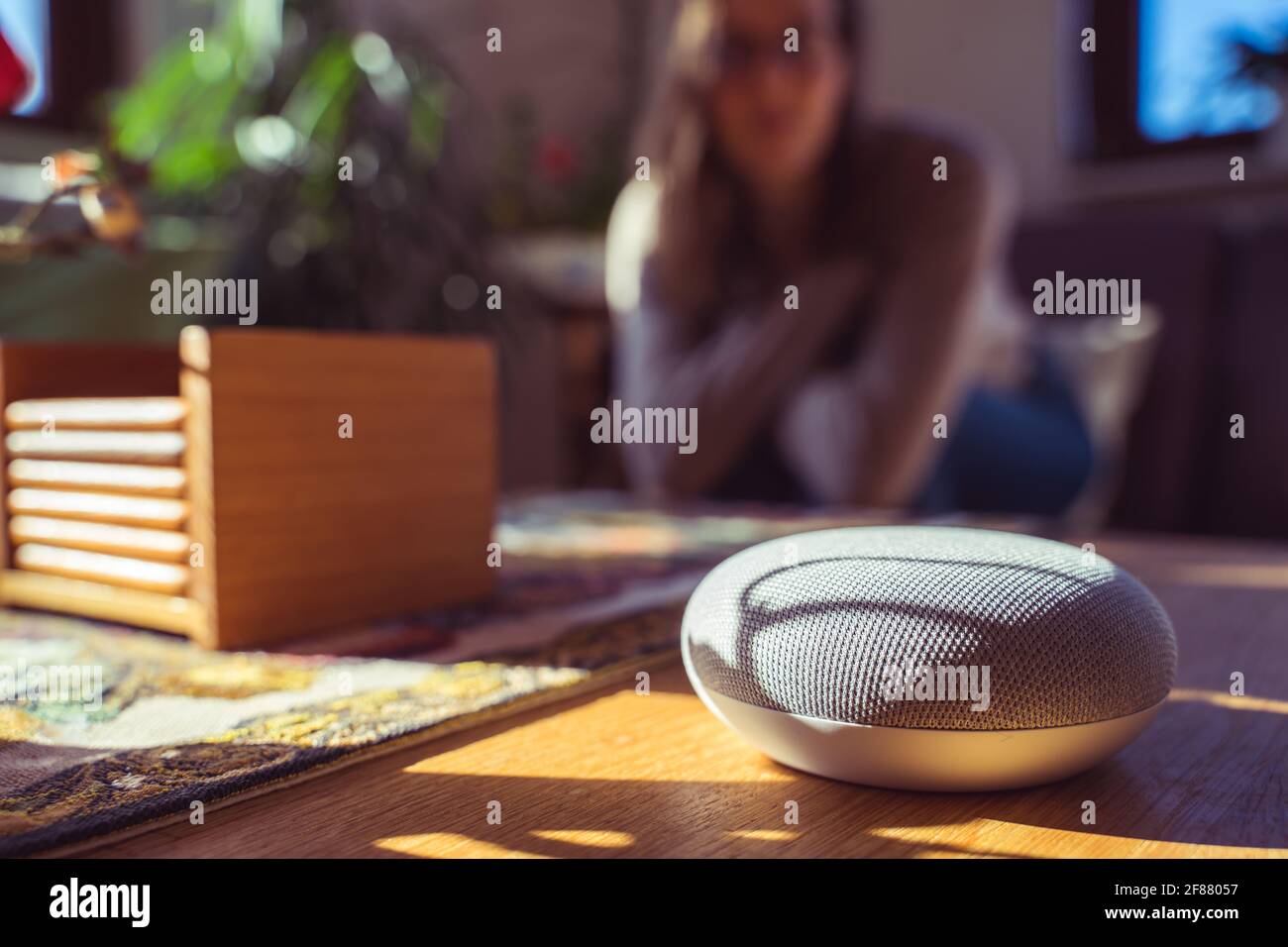 Sprachgesteuerter intelligenter Lautsprecher mit einer Frau im Hintergrund in einer Innenraumumgebung. Intelligentes AI-Lautsprecherkonzept Stockfoto