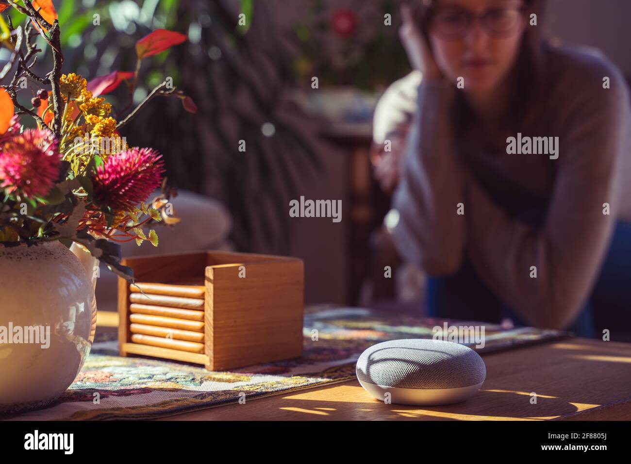 Sprachgesteuerter intelligenter Lautsprecher mit einer Frau im Hintergrund in einer Innenraumumgebung. Intelligentes AI-Lautsprecherkonzept Stockfoto