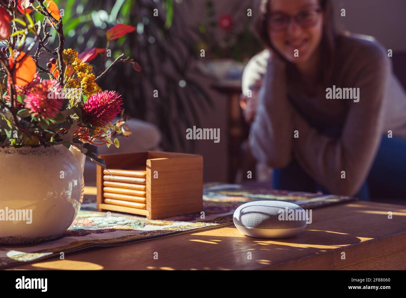 Sprachgesteuerter intelligenter Lautsprecher mit einer Frau im Hintergrund in einer Innenraumumgebung. Intelligentes AI-Lautsprecherkonzept Stockfoto