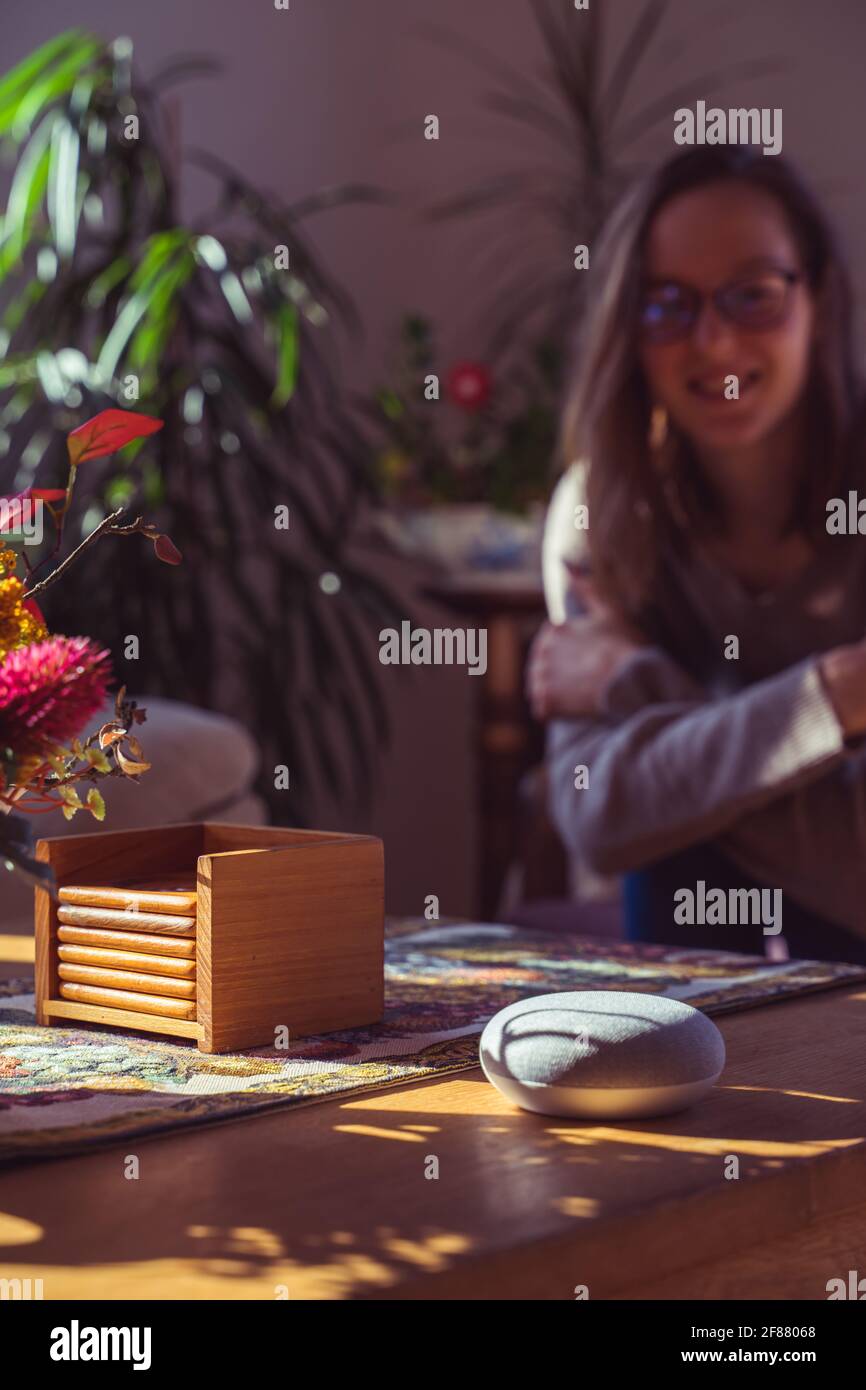Sprachgesteuerter intelligenter Lautsprecher mit einer Frau im Hintergrund in einer Innenraumumgebung. Intelligentes AI-Lautsprecherkonzept Stockfoto