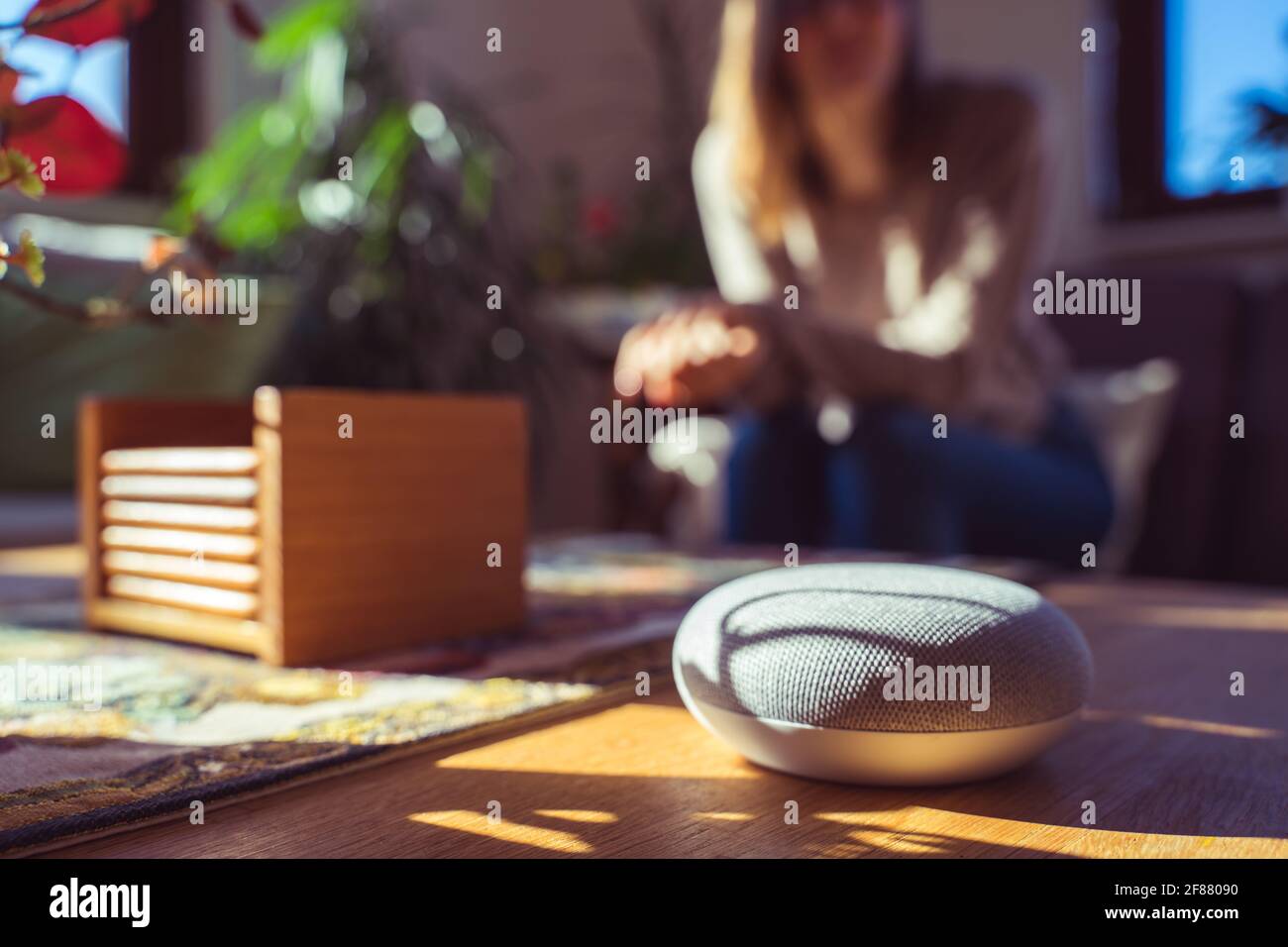 Sprachgesteuerter intelligenter Lautsprecher mit einer Frau im Hintergrund in einer Innenraumumgebung. Intelligentes AI-Lautsprecherkonzept Stockfoto