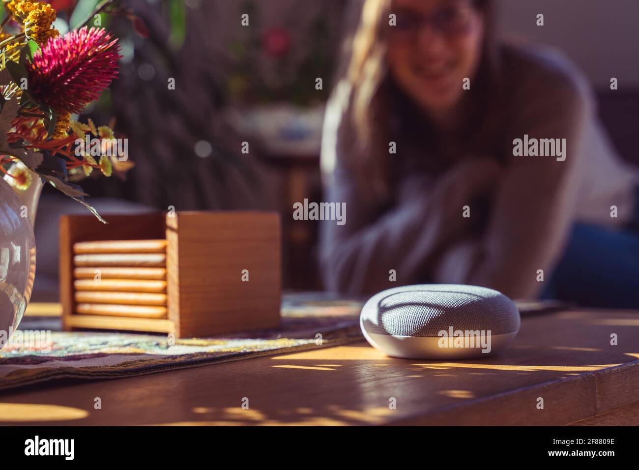 Sprachgesteuerter intelligenter Lautsprecher mit einer Frau im Hintergrund in einer Innenraumumgebung. Intelligentes AI-Lautsprecherkonzept Stockfoto