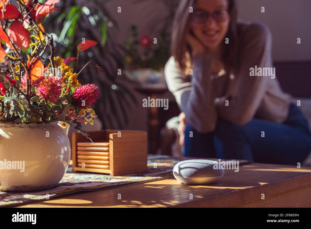 Sprachgesteuerter intelligenter Lautsprecher mit einer Frau im Hintergrund in einer Innenraumumgebung. Intelligentes AI-Lautsprecherkonzept Stockfoto