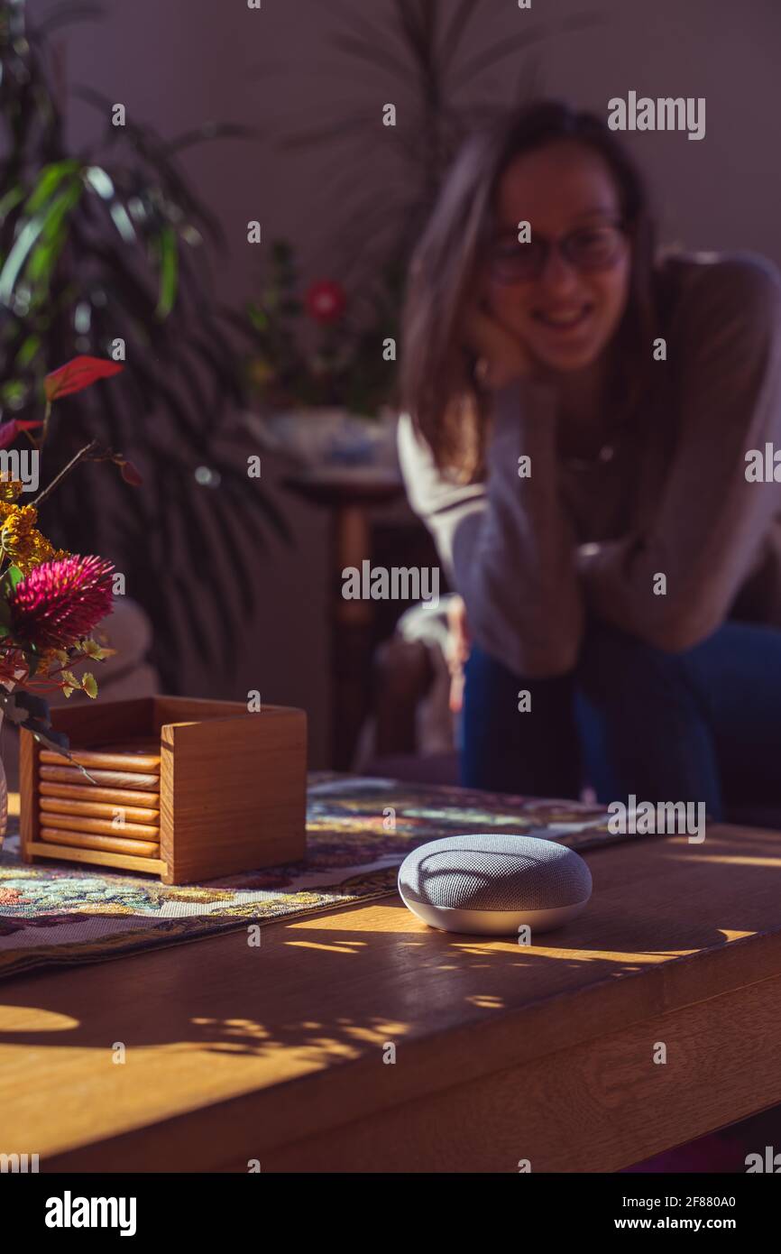 Sprachgesteuerter intelligenter Lautsprecher mit einer Frau im Hintergrund in einer Innenraumumgebung. Intelligentes AI-Lautsprecherkonzept Stockfoto