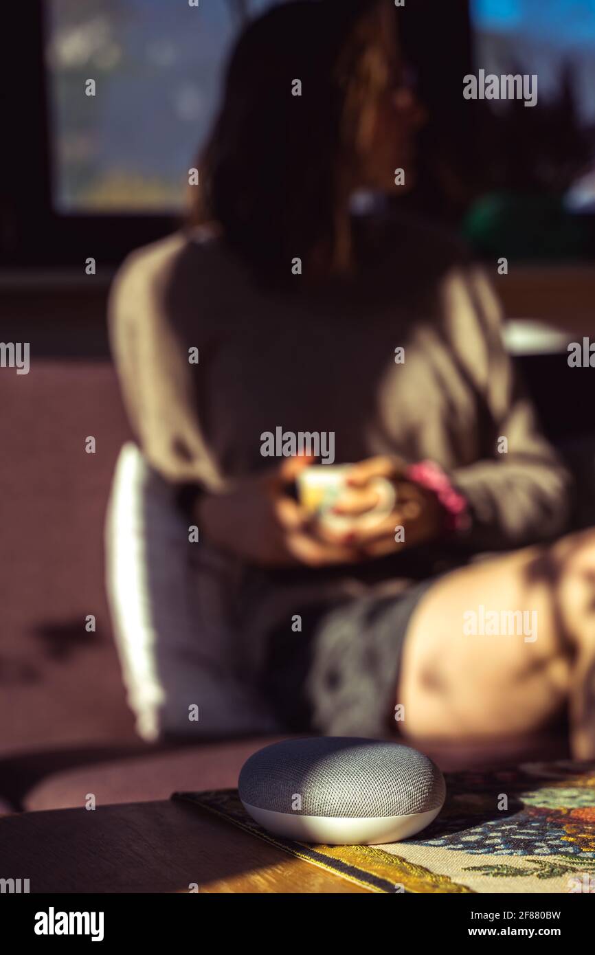 Sprachgesteuerter intelligenter Lautsprecher mit einer Frau im Hintergrund in einer Innenraumumgebung. Intelligentes AI-Lautsprecherkonzept Stockfoto