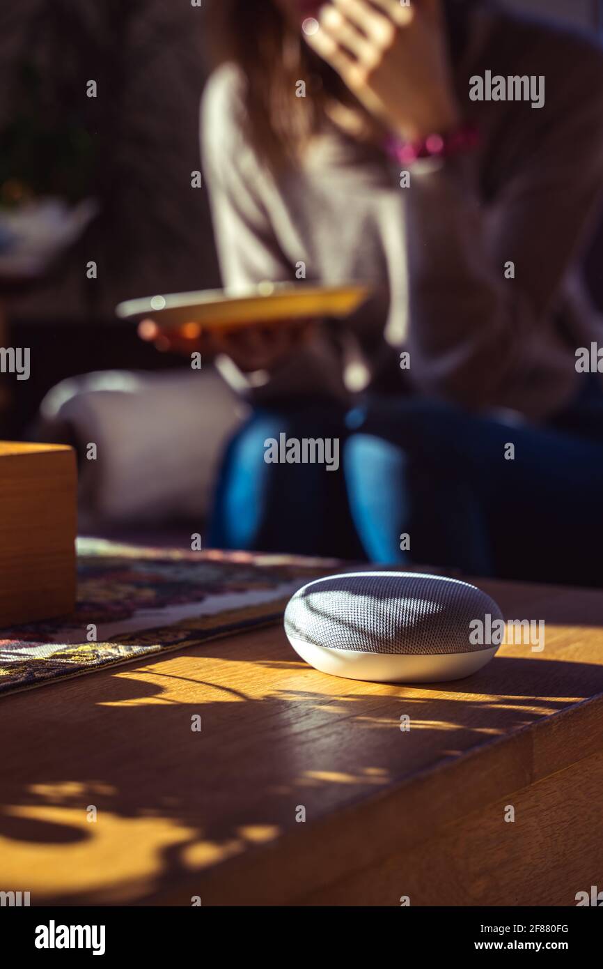 Sprachgesteuerter intelligenter Lautsprecher mit einer Frau im Hintergrund in einer Innenraumumgebung. Intelligentes AI-Lautsprecherkonzept Stockfoto